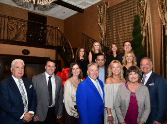 A group of professionally dressed Township staff and elected officials pose together inside an ornate interior space with a curved staircase, decorative railings, tall draped windows, and a chandelier visible in the background. The group is arranged in rows and smiling toward the camera. 